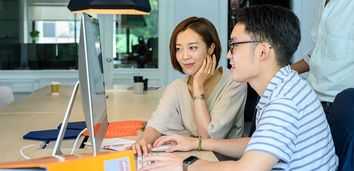 Man and woman watching computer A woman sitting at the computer with another man.